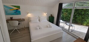 A bedroom with a bed, a desk, a chair, a green cabinet, and a view of greenery through a glass door. - Villa Blanche - Entre montagne, piscine et calme (Sévrier)