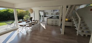 A modern kitchen with a central island, a dining area with a table and chairs, and a staircase leading to an upper level. - Villa Blanche - Entre montagne, piscine et calme (Sévrier)