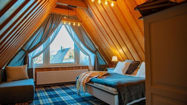 A cozy attic bedroom with a bed, a chair, and a window with curtains.