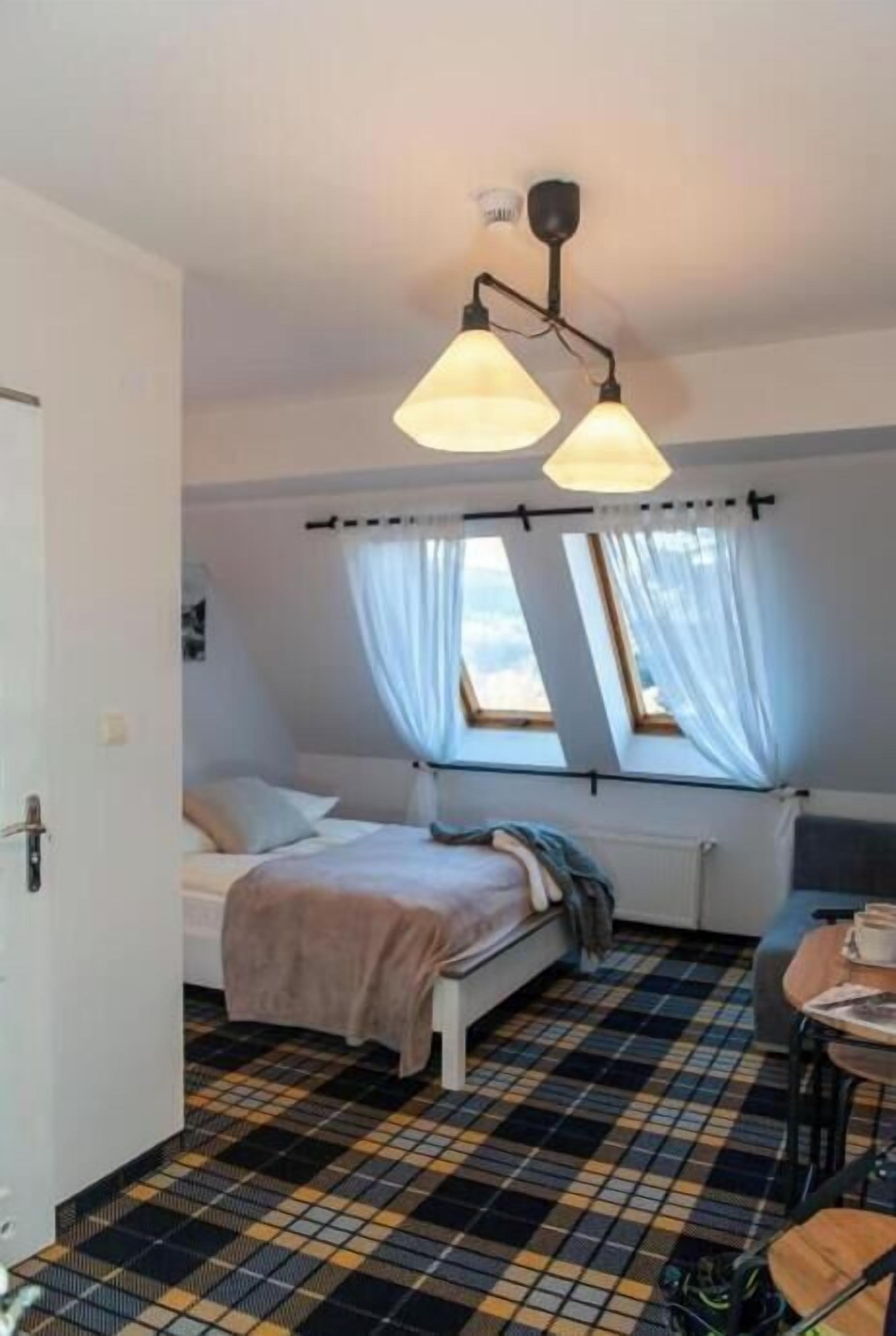 A room with a bed, a window with curtains, a radiator, and a checkered floor.