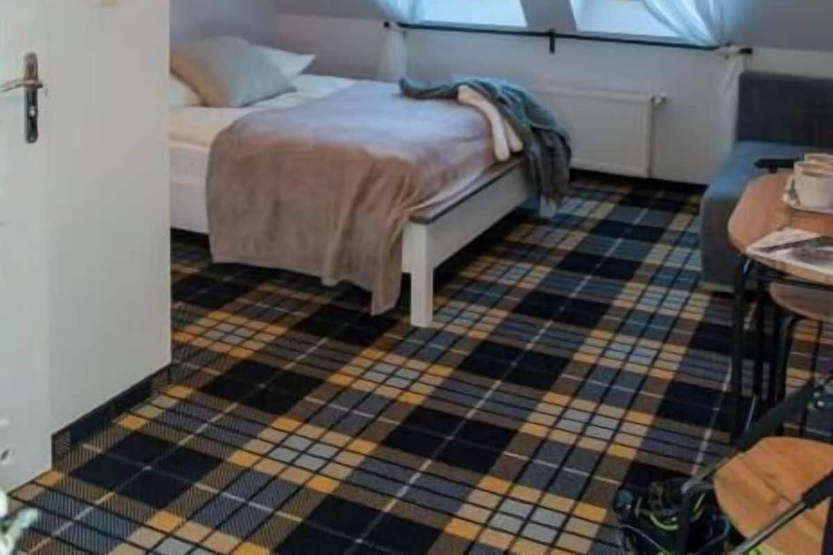Quarto com cama, janela com cortinas, radiador e chão xadrez.