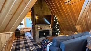 A cozy loft-style room with a checkered floor, a sofa, a fireplace, and a Christmas tree.