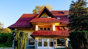 A two-story house with a red roof, a balcony, and a front porch.