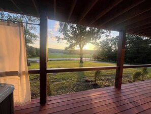 A wooden deck with a view of a grassy field and a tree.