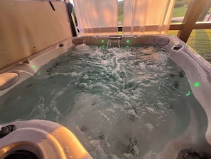 A hot tub with water jets, surrounded by a wooden deck and a white curtain.
