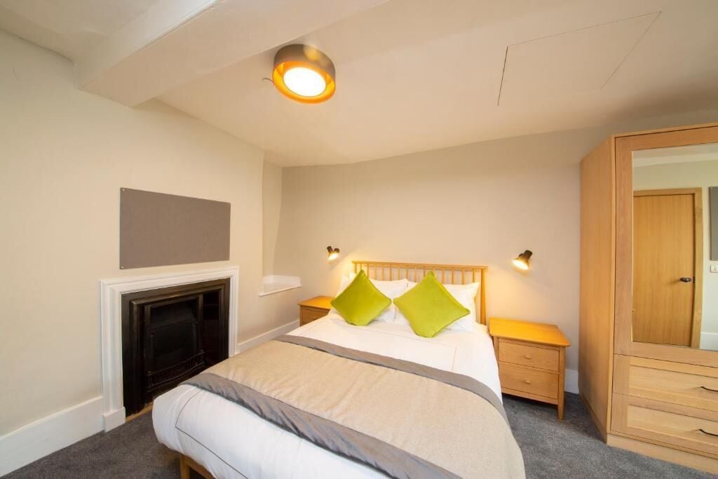 A bedroom with a bed, bedside tables, a wardrobe, a fireplace, and a wall-mounted TV.