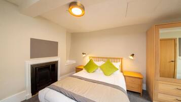A bedroom with a bed, bedside tables, a wardrobe, a fireplace, and a wall-mounted TV.