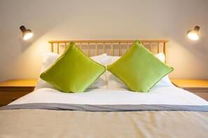 Ein Bett mit Holz Kopfteil, zwei grüne Kissen, weißer Bettwäsche und zwei Nachttischlampen.