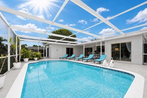 Une piscine avec des chaises longues, un patio couvert et un ciel d’un bleu limpide.
