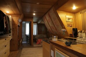 A wooden interior with a kitchen area, a dining table, and a bed in the background.