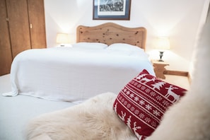 Ein Bett mit Holz-Kopfteil, weißer Bettwäsche und einem roten Kissen mit Muster.