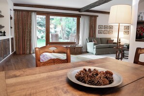 Ein Essbereich mit einem Holztisch, einer Schüssel mit Kiefernzapfen und Blick auf einen Garten durch ein großes Fenster.