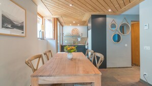 Una mesa de comedor de madera con sillas, un florero con flores y una cocina al fondo con un lavabo y armarios.