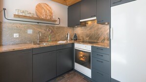 Una cocina moderna con armarios oscuros, horno empotrado y pileta de acero inoxidable.