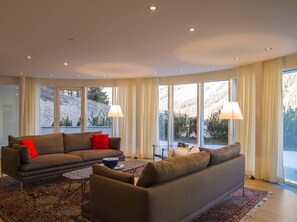 Ein modernes Wohnzimmer mit einer Couch, einem Couchtisch und Blick auf eine Berglandschaft durch große Fenster.
