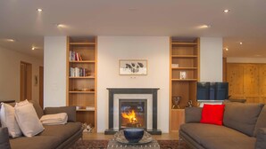 A living room with a fireplace, two sofas, a coffee table, and bookshelves. - Residenza Alpenrose 31 – Spacious 4.5-room flat with a terrace and mountain view (Sils / Segl Maria)