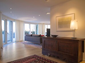 Ein geräumiges Wohnzimmer mit einer Couch, einem Holzkasten und einem großen Fenster.