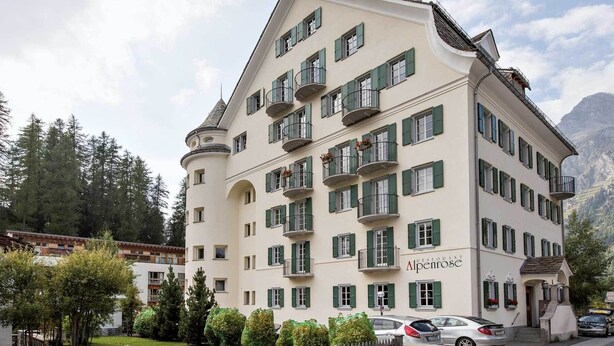 A multi-story hotel with balconies, a sign reading 'Alpenrose,' and a mountainous backdrop. - Residenza Alpenrose 31 – Spacious 4.5-room flat with a terrace and mountain view (Sils / Segl Maria)