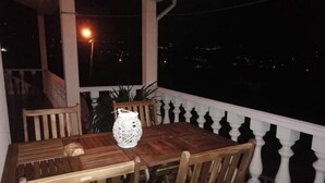 Een houten tafel met stoelen op een balkon, met een balustrade, een bloempot en een witte lantaarn.