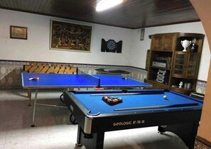Una sala de billar con dos mesas de pool, un dardo y una estantería.