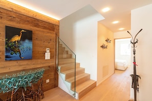 Eine Holzwand mit einem gerahmten Bild, ein Glastisch mit einer Pflanze, eine Treppe und ein Kleiderhaken mit einem Hirschkopf.
