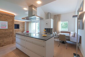 Eine moderne Küche mit einer zentralen Kochinsel, einem Essbereich mit einer Couch und einem großen Fenster, das für natürliches Licht sorgt.