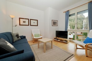 Ein Wohnzimmer mit einer Couch, einem Sessel, einem Couchtisch, einem Fernseher und gerahmten Bildern an der Wand.
