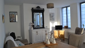 Ein Wohnzimmer mit Couchtisch aus Holz, weißen Schränken, einem großen Spiegel und einem Fernseher auf einem Holzgestell.