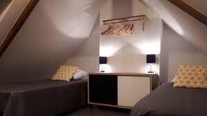 Ein kleines, dreieckiges Schlafzimmer im Dachgeschoss mit zwei Betten, einem Schminktisch und einer Kleiderstange.