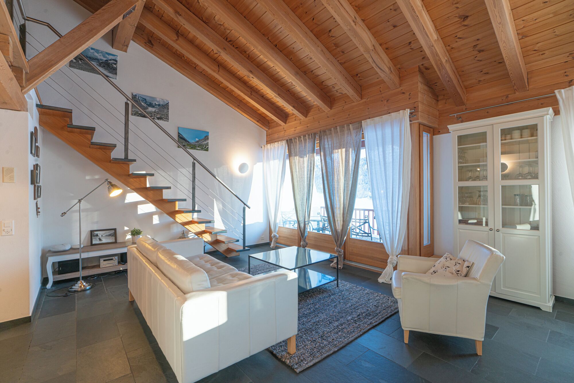 Un salon moderne avec un escalier en bois, des meubles blancs et une table basse en verre.