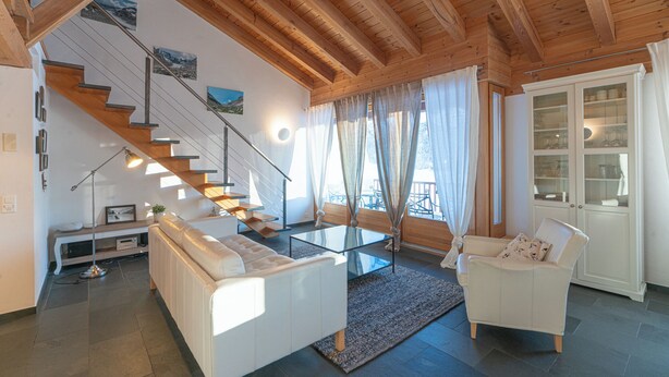 Ein modernes Wohnzimmer mit einer Holztreppe, weißen Möbeln und einem Glastisch.