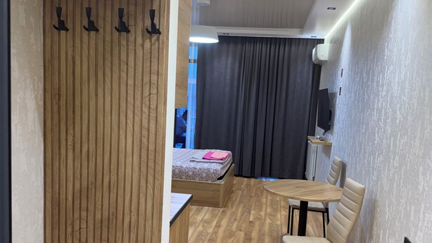 A modern room with a wooden wardrobe, a bed, a dining table with chairs, and a TV on the wall. - Fantastico (Batumi)