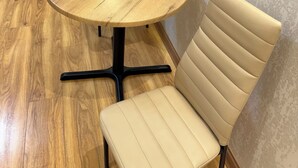 A round wooden table with a black metal base, two beige chairs, a television on a stand, and a curtain in the background. - Fantastico (Batumi)