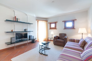 A living room with a sofa, armchair, TV, and shelves. - Chesa Polaschin – Bright Apartment with a Balcony & Prime Location (Sils/Segl Maria)