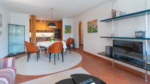 Un salon moderne comprenant un coin repas, une cuisine et un téléviseur posé sur un meuble.