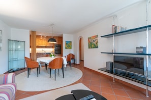 A modern living room with a dining area, kitchen, and a TV on a stand. - Chesa Polaschin – Bright Apartment with a Balcony & Prime Location (Sils/Segl Maria)