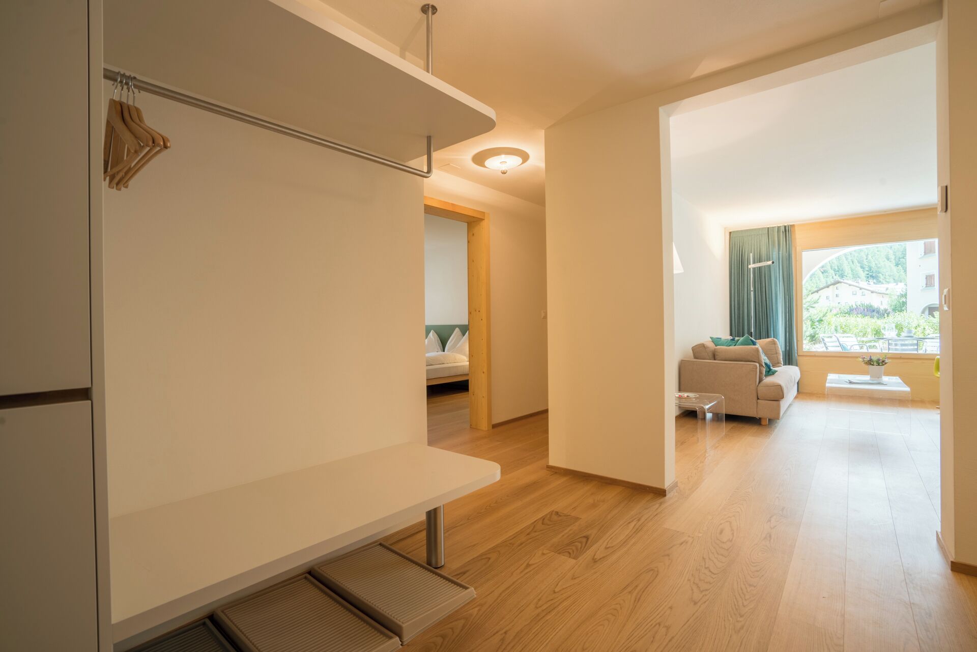 A modern interior with a wooden floor, a sofa, a dining table, and a view of greenery outside.