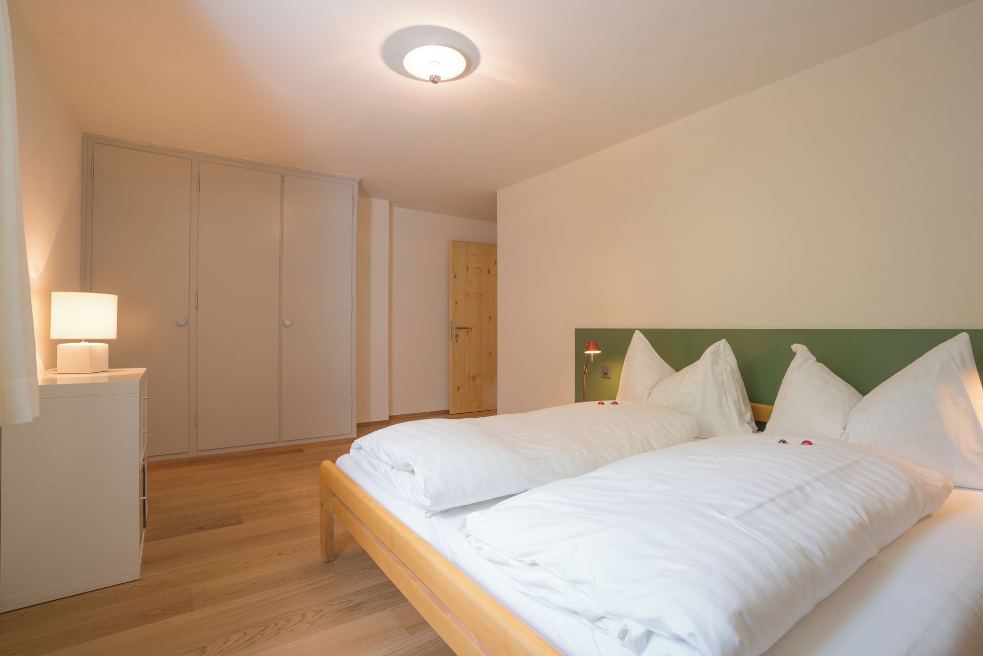 Ein Schlafzimmer mit Bett, Nachttischen, einem Kleiderschrank und einer Deckenleuchte.