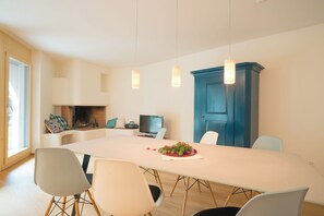 Ein moderner Essbereich mit einem langen Tisch, Stühlen, Pendelleuchten, einem blauen Schrank und einem Kamin.