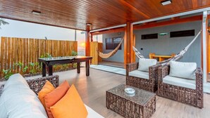 Un patio exterior con mobiliario de mimbre, una hamaca y techo de madera.