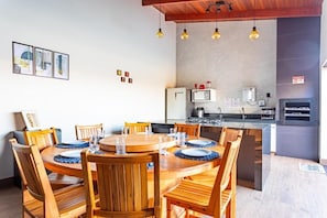 Een eetgedeelte met een houten tafel en stoelen, een keuken met moderne apparatuur, en uitzicht op de omgeving.