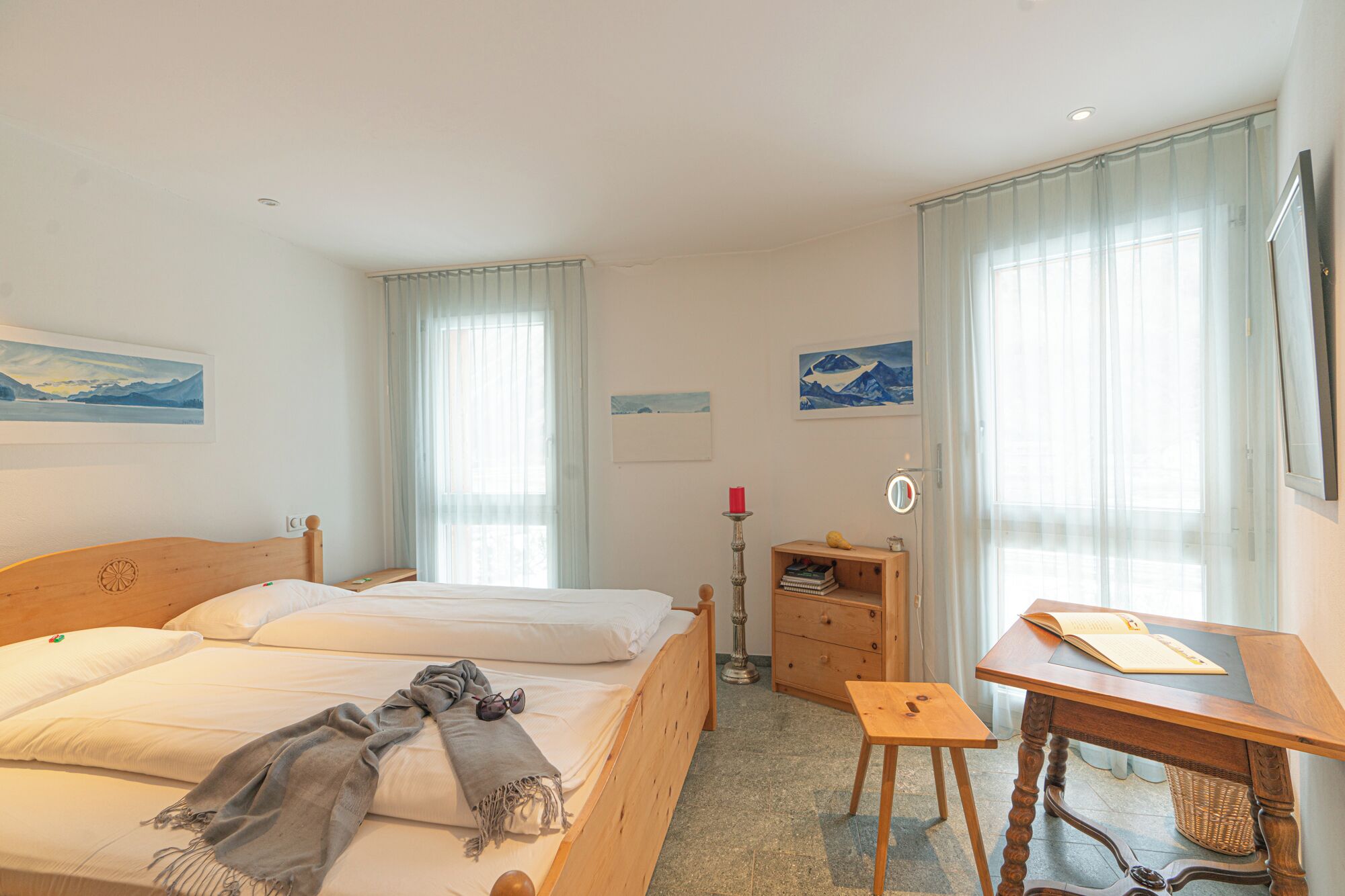 Et hotelværelse med to senge, et træskrivebord, et lille bord og et spejl.