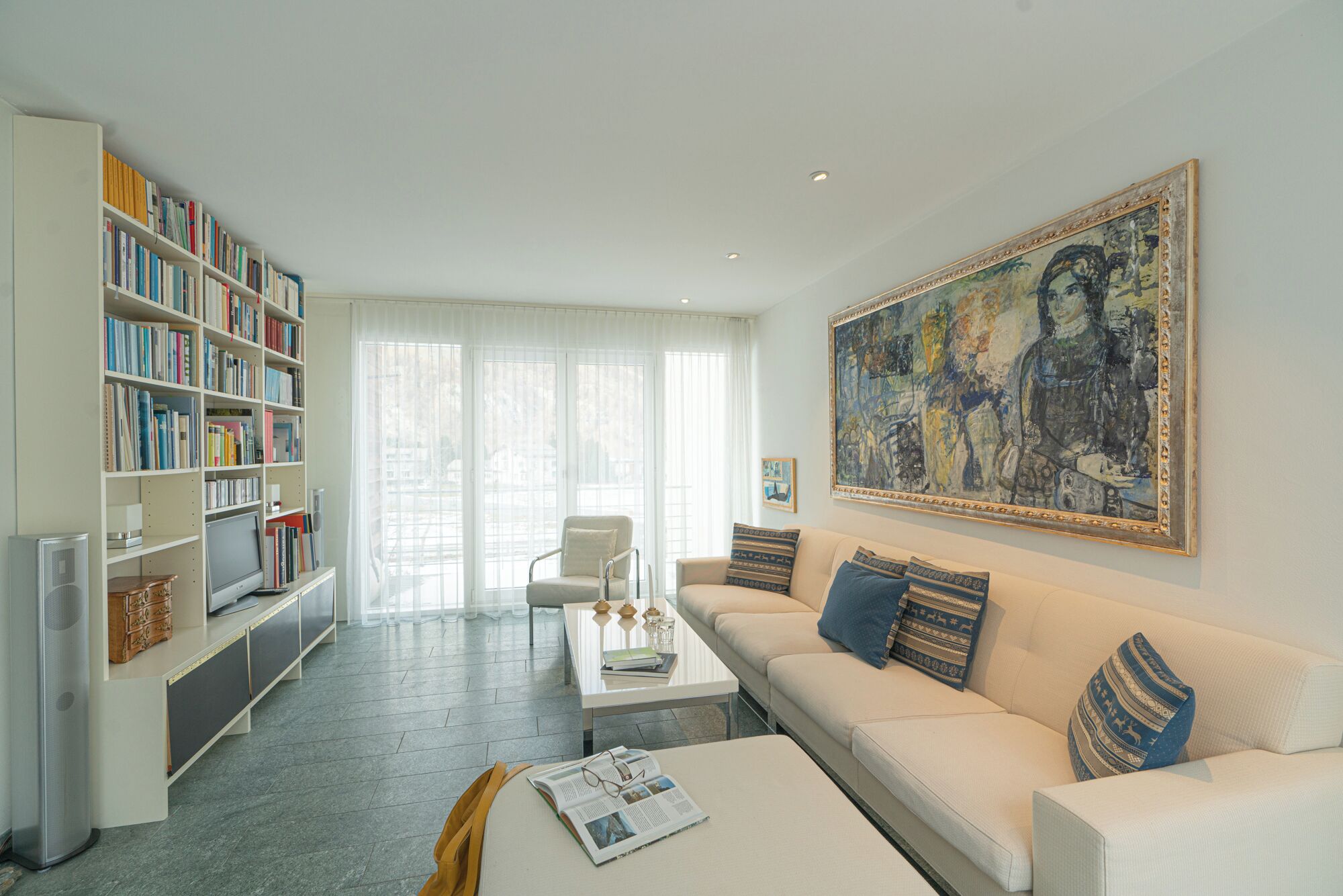 Un salon avec un canapé, une table basse, une bibliothèque et un tableau accroché au mur.