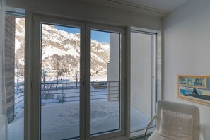 Ein Zimmer mit einer großen Schiebeglaswand, die zu einer verschneiten Außenanlage mit Bergen im Hintergrund führt.