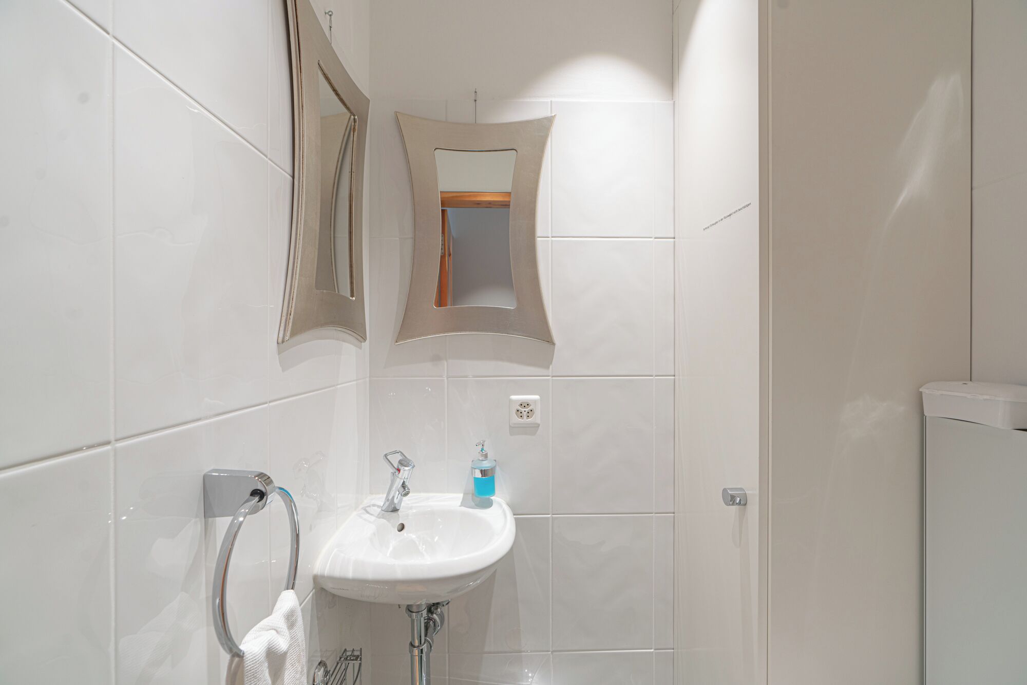 Un baño con lavamanos blanco, espejo y barra para toallas.