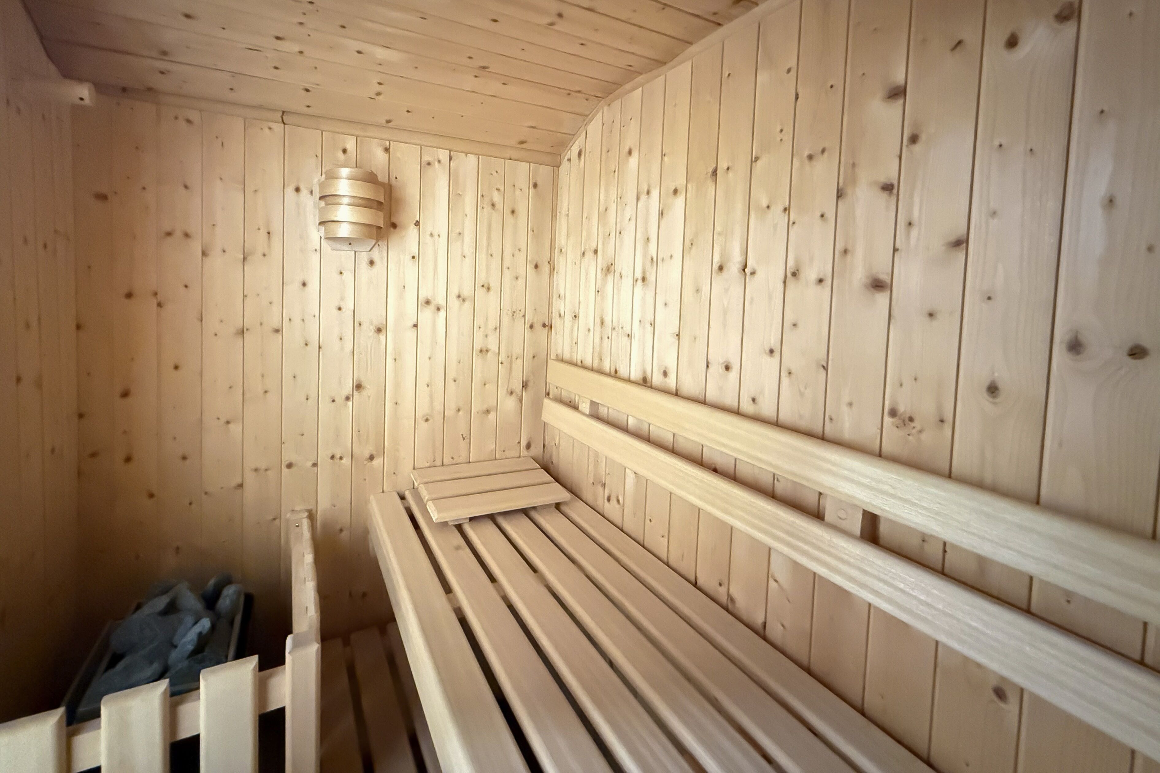 Un sauna en bois, doté de bancs et d’un luminaire au plafond.