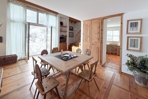 Ein Essbereich mit Holztisch und -stühlen, einem großen Fenster mit Vorhängen und einer Treppe zu einem anderen Raum.