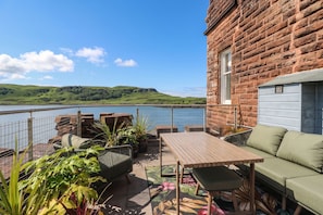 A patio with outdoor furniture, a table, and a sofa overlooking a lake. - Heather Island View (Oban)