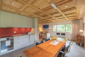 Eine moderne Küche mit Holzbalken, einem Essbereich mit Holztisch und Blick ins Freie durch große Fenster.