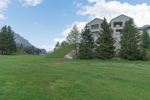A two-story building with a stone facade, surrounded by trees and a grassy field. - Chesa Piol Studio – Modern Studio with a View & Wellness Facilities (Maloja)